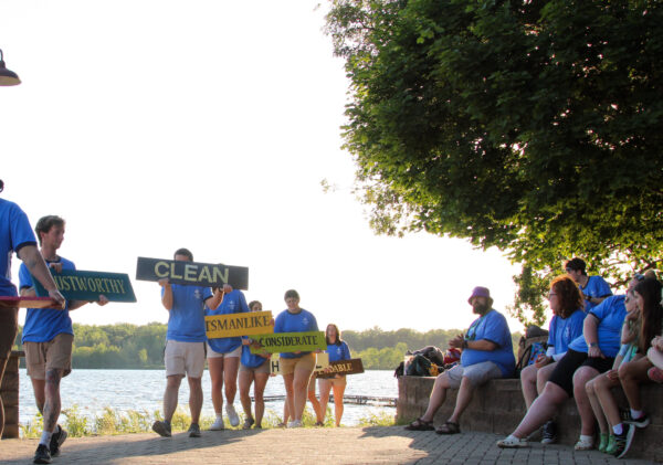 Camp counselors walking out with signs that say the core values of Camp Crosley.