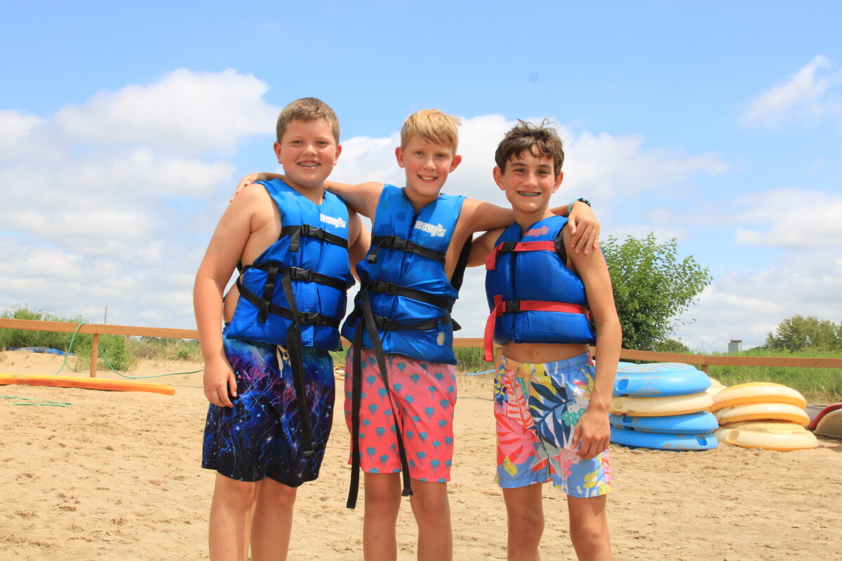 Three boys posing for a photo together at the beach.