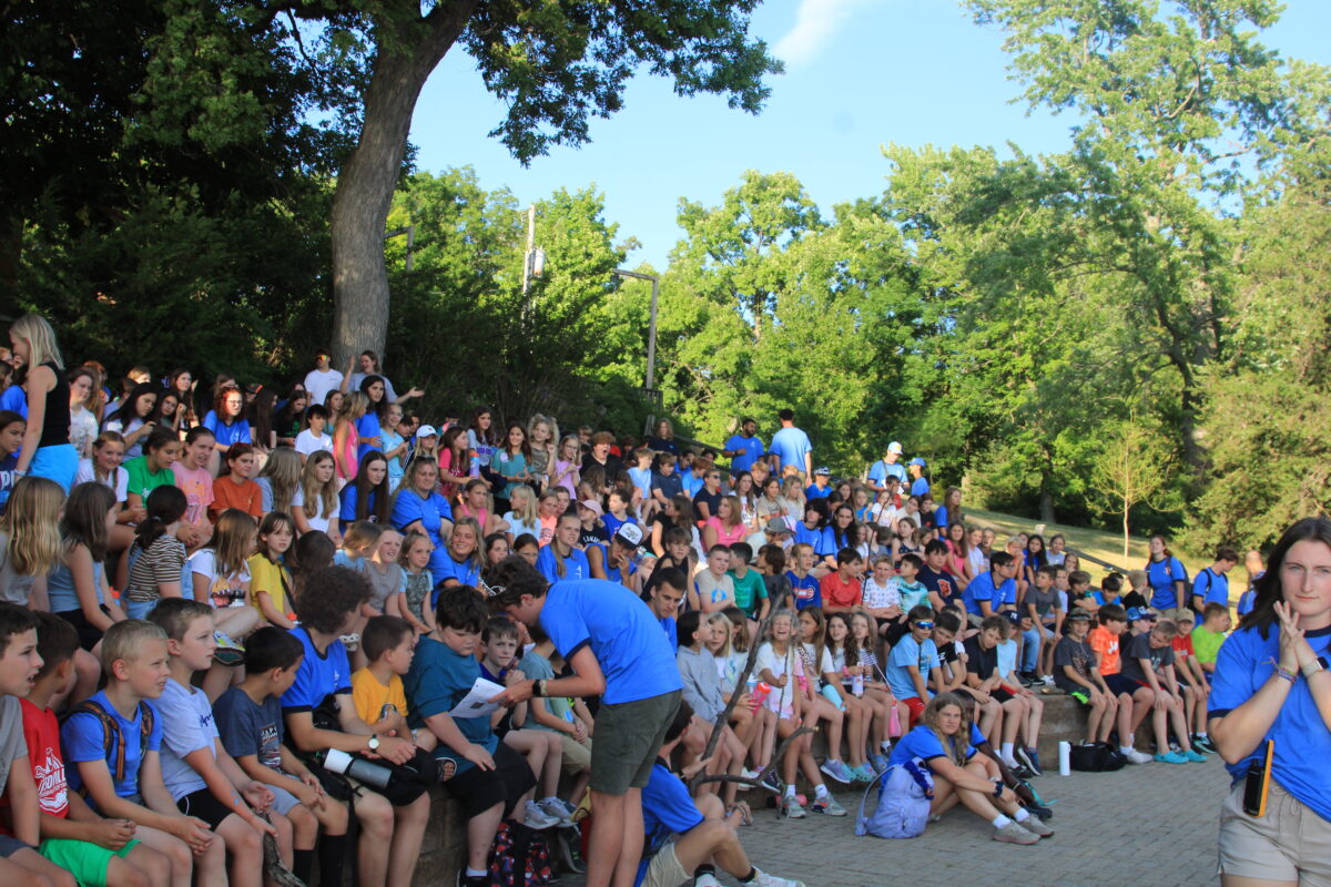 A large group of campers sit together at camp orientation on day one of summer camp.