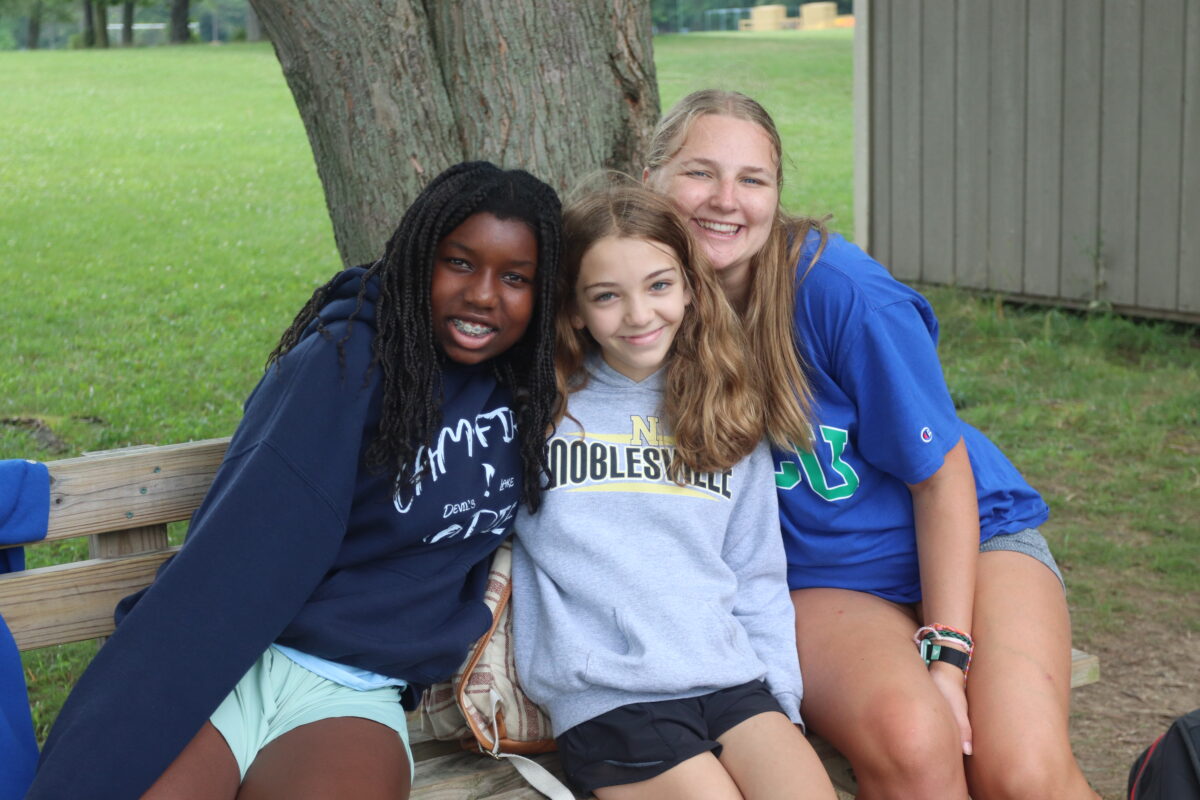 Three girls sitting on a bench posing for a photo together.