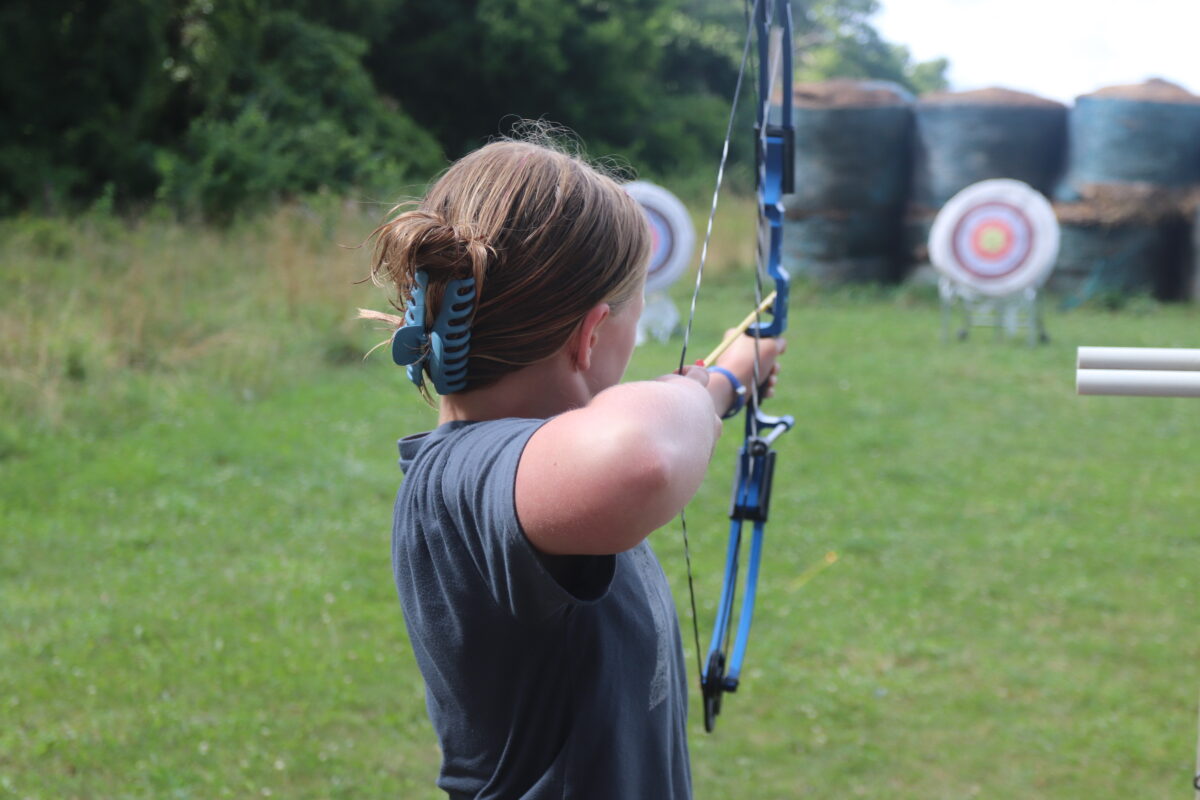 A young girl about to shoot a bow and arrow at a target.