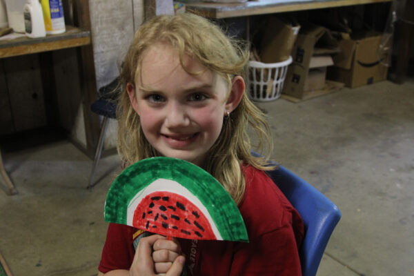 Young girl holding up a handmade watermelon fan.
