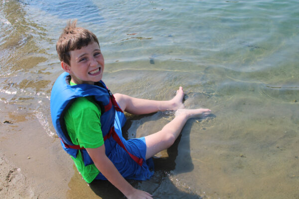 Young boy sitting on the beach in a life jacket.